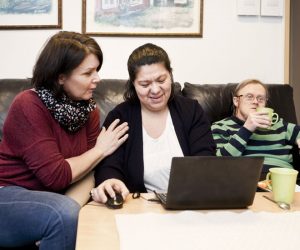 Healthcare worker helping woman with down syndrome in using laptop while man having drink at sofa